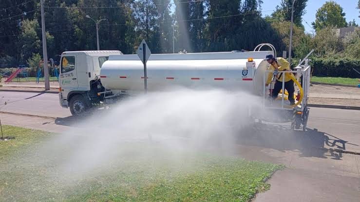 Camión aljibe regando el pasto de un área verde urbana.